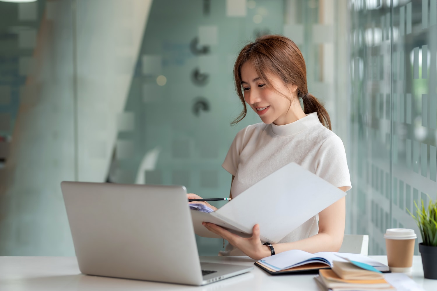 Beautiful Young Asian businesswoman holding documents to checking authenticity the laptop is placed at the office table. coding-API-signature-screen