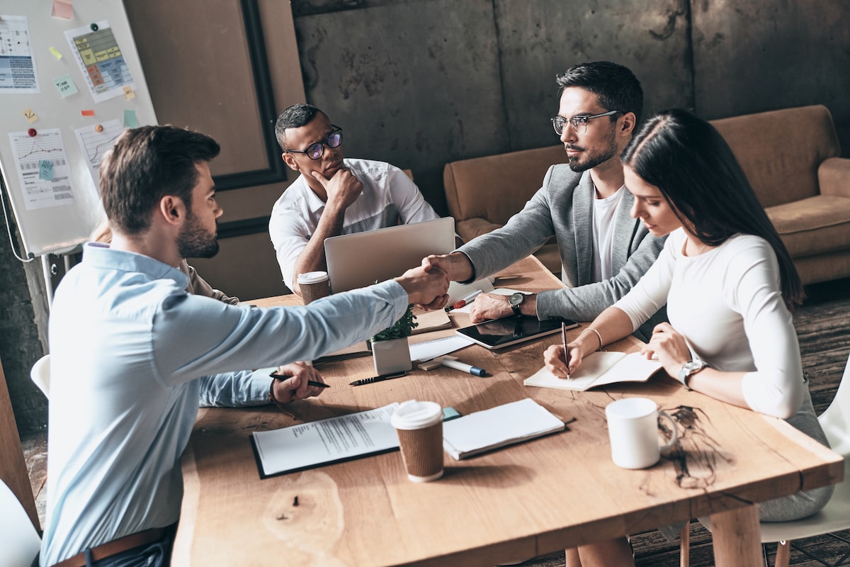Great job! Top view of young modern men in smart casual wear shaking hands while working in the creative office