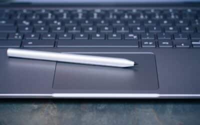 Un stylet argenté repose sur le pavé tactile d'un ordinateur portable sombre, évoquant la signature électronique et l'innovation en entreprise.