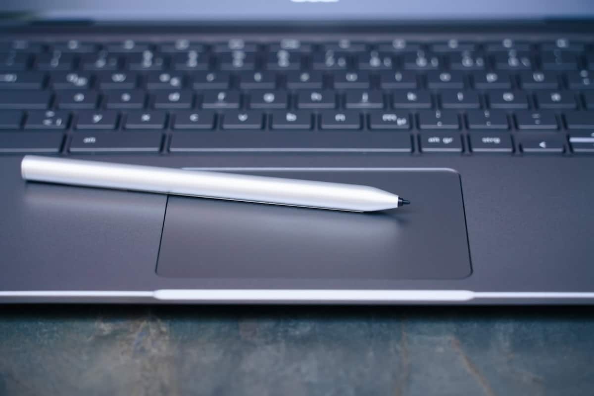 Un stylet argenté repose sur le pavé tactile d'un ordinateur portable sombre, évoquant la signature électronique et l'innovation en entreprise.